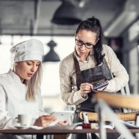 Female chef and waitress with iPad and calculator. Photo.